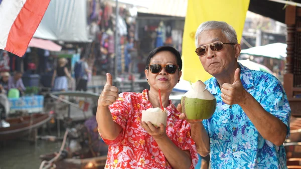 Casal sênior asiático bebendo suco de coco no mercado flutuante. Viajar para Tailândia — Fotografia de Stock