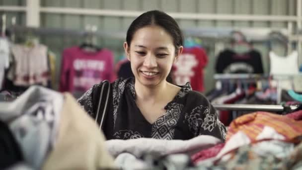 Happy Asian mixed race girl looking for good cheap clothes in sale bazaar — ストック動画