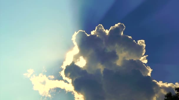 Λαμπερό ήλιο ακτίνες ακτίνες δείχνουν πίσω από το μεγάλο λευκό σύννεφο σε φόντο μπλε του ουρανού — Αρχείο Βίντεο