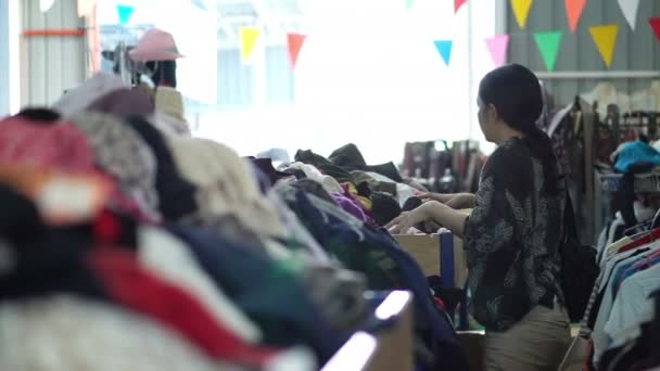 Asiático misto mulher compras segunda roupa no mercado de pulgas armazém — Vídeo de Stock