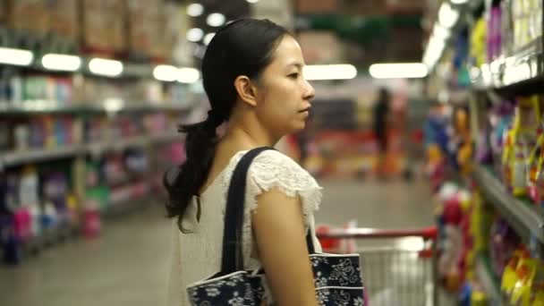Menina asiática seleciona itens no hipermercado, prateleiras de supermercado — Vídeo de Stock