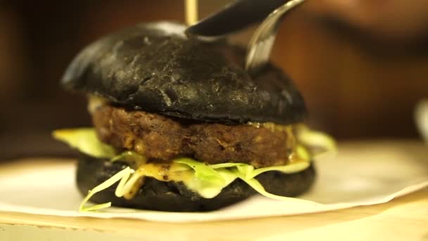 Hamburguesa de carbón negro con salsa roja cortada. Nueva tendencia comida negra saludable — Vídeo de stock