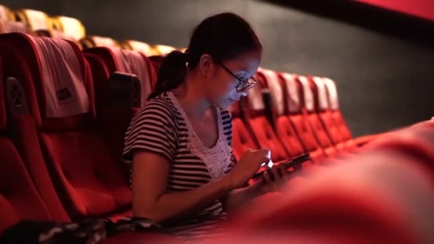 Aziatische vrouw met behulp van mobiele telefoon in een lege bioscoop theater. Zet uw telefoon vóór film concept — Stockvideo