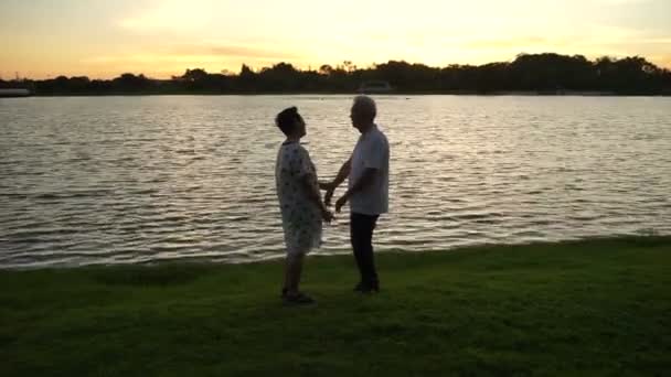 Ázsiai idősebb pár együtt reggeli fényben arany sunrise tó mellett gyakorolják. — Stock videók