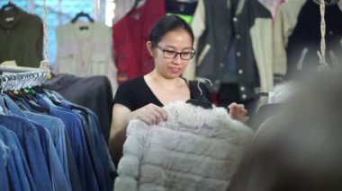 Asyalı kadın alışveriş, raf üzerinde giysiler seçmek ve beyaz ceket deneyin