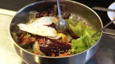 Bibimbap Korece pirinç ve paslanmaz kaşık kullanarak çeşitli sebze gıda kapları karıştırma