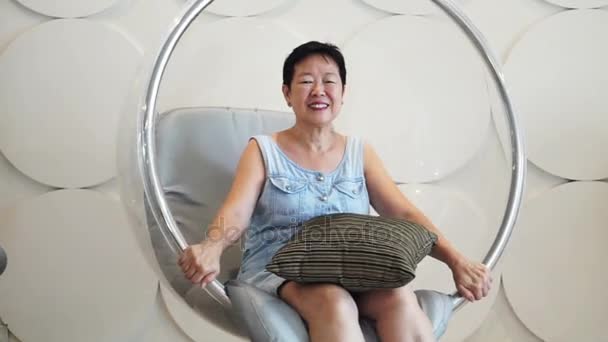 Asiatisk senior kvinna sitta och koppla av i loungen på transparent flytande boll stol — Stockvideo