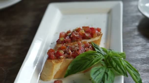 Mains prenant une délicieuse bruschetta et des feuilles de basilic frais à manger — Video