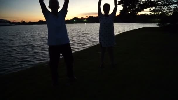 Asian senior couple exercise together at morning dawn lake — Stock Video
