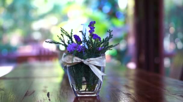 Flor violeta e vaso de vidro decorar em mesa de madeira no jardim — Vídeo de Stock