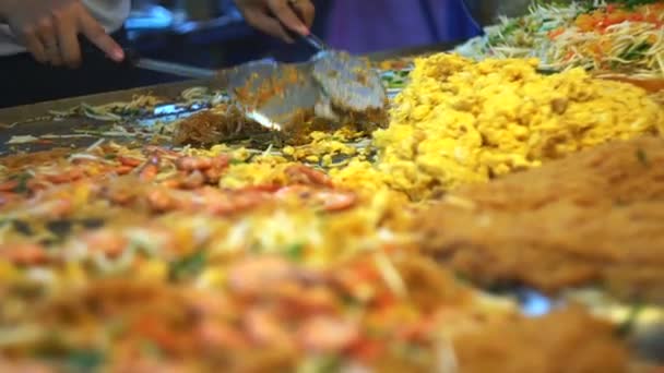 Hand cooking Pad Thai on big pan at local street market. Stir-fried pink color noodles in slow motion — Stock Video