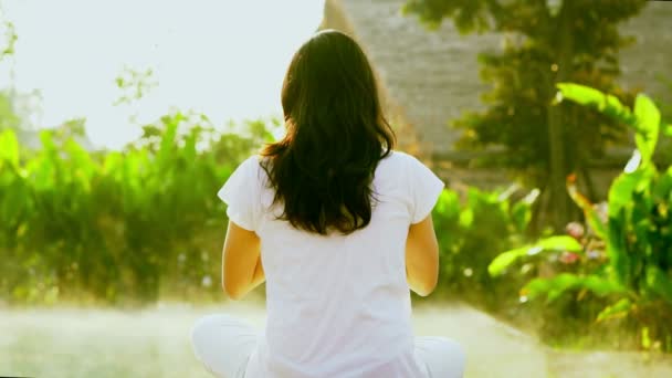 Asian girl exercise yoga next to wellness spa pool in the sun with green background and morning fog slow motion shot — Stock Video