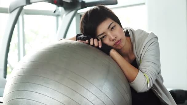 Cabello corto chica asiática en el gimnasio con bola de yoga tiro. Cansado agotado pero aún sonriendo — Vídeo de stock