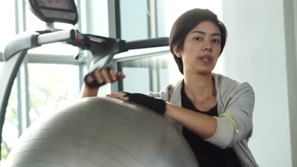 Cabello corto chica asiática en el gimnasio con bola de yoga tiro. Cansado agotado pero aún sonriendo — Vídeos de Stock