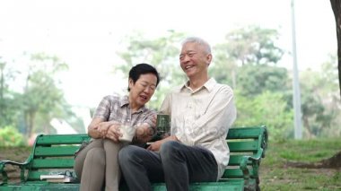 Oturma ve çay, sabah parkta kahve içme ağır çekim mutlu Asya kıdemli çift. Konuşmayı ve sevgi gösteren