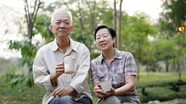 Antiguo asiática pareja mayor mañana fecha con taza de café verde fondo parque — Foto de Stock
