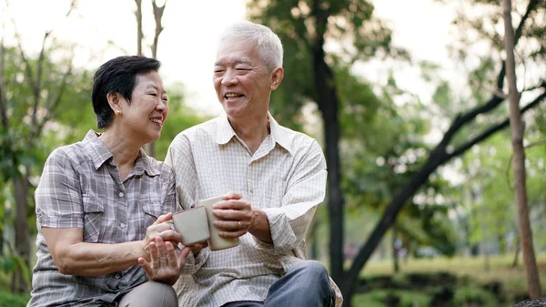 Утреннее свидание пожилой азиатской пары с чашкой кофе на зеленом фоне парка — стоковое фото