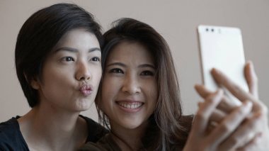 Two mixed race Asian girls taking selfie with smart phone clipart