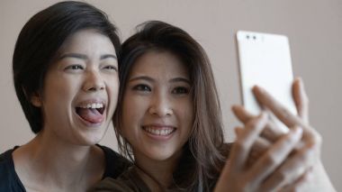 Two happy photogenic Asian womans talking selfie with phone clipart