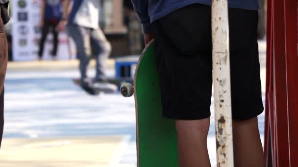 Ein Mann spielt Skateboard im Hintergrund des Parkboards, mit einem Freund im Vordergrund, der das Brett hält und ihn ansieht — Stockvideo