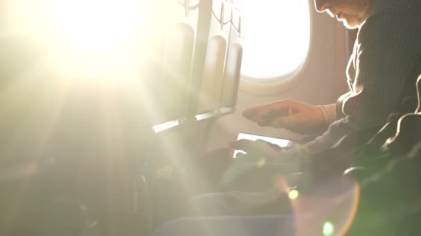 Coucher de soleil par la fenêtre de l'avion. Homme utilisant une tablette pendant un vol international — Video
