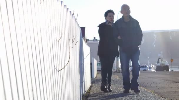 Asian senior couple walking together in Europe trip. Morning sun and house white fence — Stock Video