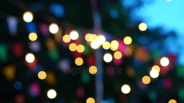 Blur luz de fondo bokeh de bombillas del festival de la noche y banderas de colores en el cielo azul hora mágica — Vídeos de Stock