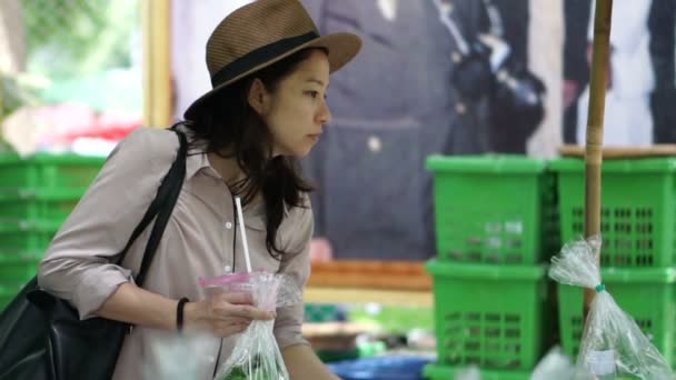 Ázsiai nő mosolyogva a viselt kalap a helyi mezőgazdasági termelő piac területén. Keres, és felvette a friss, bio zöldség — Stock videók