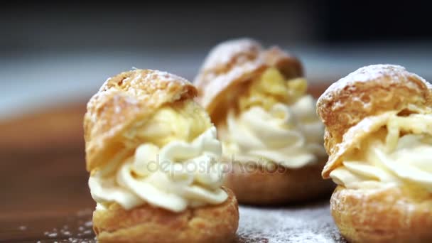Piekarnia piekarz zraszanie proszkowane cukru choux cream puff na pokładzie drewna 4k — Wideo stockowe