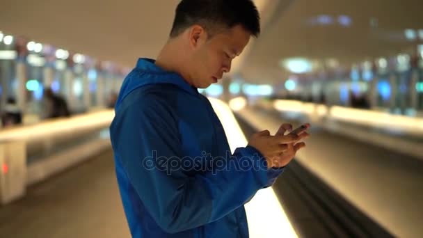 Ασίας backpacker άνθρωπος τον έλεγχο χρησιμοποιώντας έξυπνο τηλέφωνο στο αεροδρόμιο μετά την προσγείωση τη νύχτα — Αρχείο Βίντεο