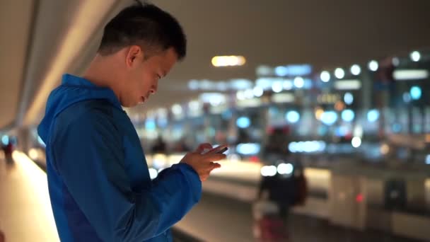 Ασίας backpacker άνθρωπος τον έλεγχο χρησιμοποιώντας έξυπνο τηλέφωνο στο αεροδρόμιο μετά την προσγείωση τη νύχτα — Αρχείο Βίντεο