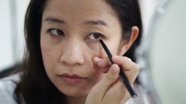 Asyalı kadın yapmak yapıyor, göz kalemi ayna ağır çekim önünde çizim. Güzellik ve kozmetik kavramı