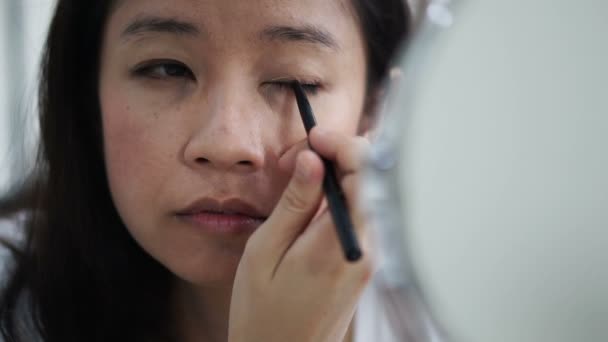 Азіатські жінки роблять make up, малювання підводка для очей перед дзеркалом повільний рух. Краси і косметичних концепції — стокове відео