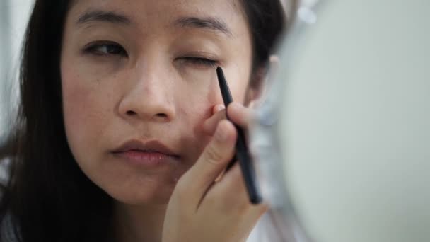Asian kobieta robi make up, rysunek eyeliner przed lustrem zwolnionym tempie. Pojęcie piękna i kosmetyczne — Wideo stockowe