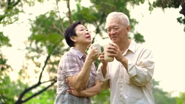 Asijské starší pár znázorňující milující a péče prostřednictvím šálek kávy v ranní světlé přírodní park — Stock video