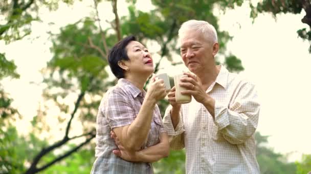 Asiatiska senior par visar tillgiven och vård genom en kopp kaffe i morgon ljusa naturpark — Stockvideo