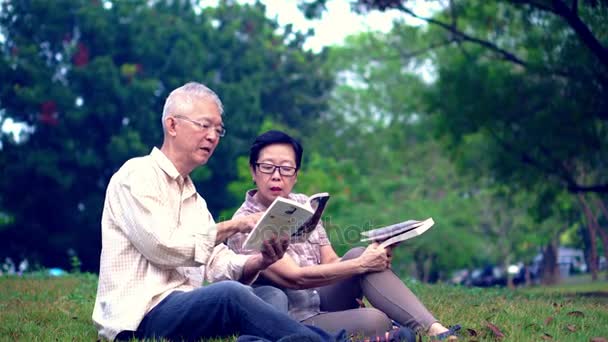 Asiatiska senior par läsa böcker på park. Tillbringa kvalitetstid och slutar aldrig lära sig något nytt — Stockvideo