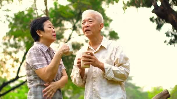 Азиатская старшая пара проявляет нежность и заботу через чашку кофе в утреннем ярком природном парке — стоковое видео