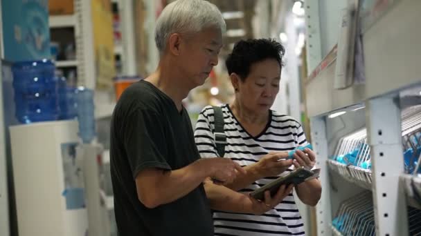 Asiática pareja de ancianos elegir tubería de agua en el centro comercial de construcción de casa. Uso de pad para buscar información en línea — Vídeo de stock