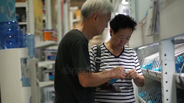 Asiática pareja de ancianos elegir tubería de agua en el centro comercial de construcción de casa. Uso de pad para buscar información en línea — Vídeo de stock