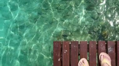 Güzel ada turkuaz açık okyanus arka plan ile ahşap güvertede ayakta turist ayakları ile sarı flip flop