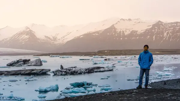 Азиатский путешественник стоит перед величественной красивой ландшафтной ледниковой лагуной Исландии — стоковое фото