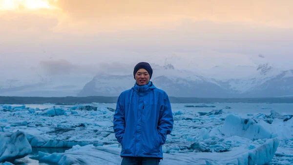 Азиатский мужчина стоит перед айсбергом миллионы лет на ледниковой лагуне Исландии — стоковое фото