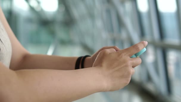 Femme utilisant un téléphone intelligent près de la fenêtre à l'aéroport, avion en arrière-plan — Video