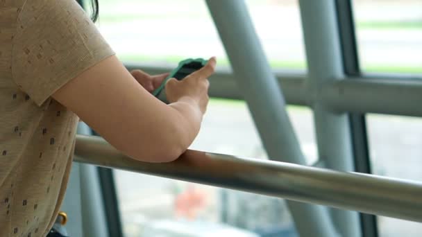 Mujer usando un teléfono inteligente junto a la ventana en el aeropuerto, plano en segundo plano — Vídeo de stock