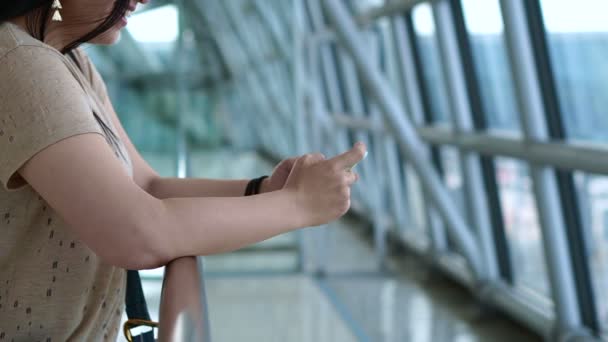 Woman using smart phone by the window at the airport, plane in background — Stock Video