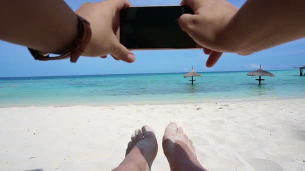 स्मार्ट फोनसह फोटो घेऊन हाताचा दृष्टीकोन. पाय आणि महासागर सुट्टी पार्श्वभूमी — स्टॉक व्हिडिओ
