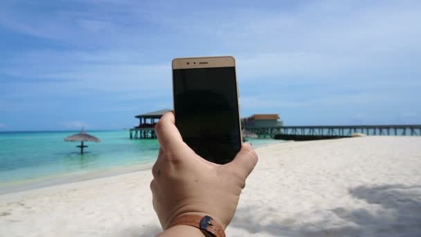 Vista panorámica de un teléfono inteligente tomando fotos en la mano del turista. Divertirse en vacaciones en el océano — Vídeo de stock