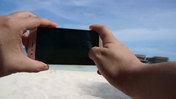 Punto di vista della mano scattare foto con lo smartphone. piedi e oceano vacanza sfondo — Video Stock