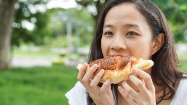 Holding ve yeşil renkli Park'ta taze pişmiş ekmek ekmek yeme Asyalı kadın